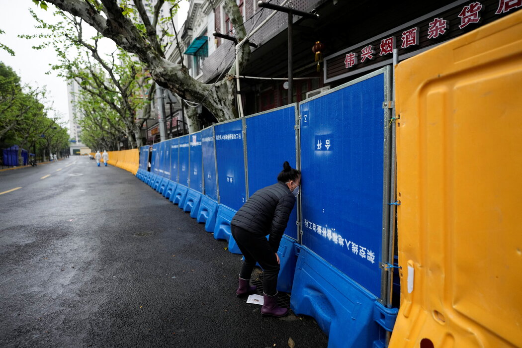 上海封锁期间，一名女子在封闭区域试图透过缝隙向摊贩购买食物